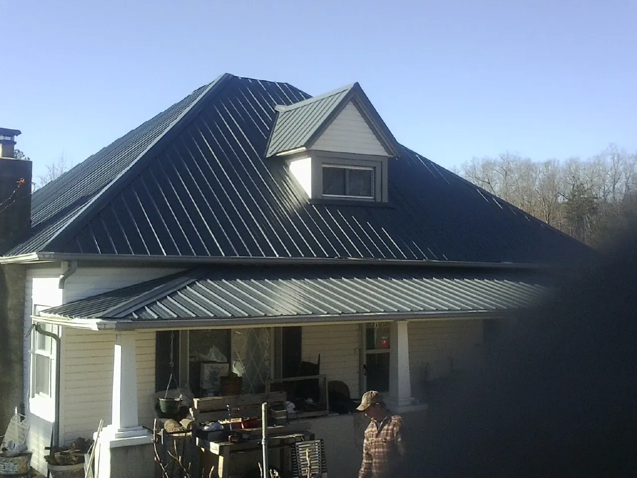 Dark blue standing seam metal roof with a dormer above a front porch in Genoa