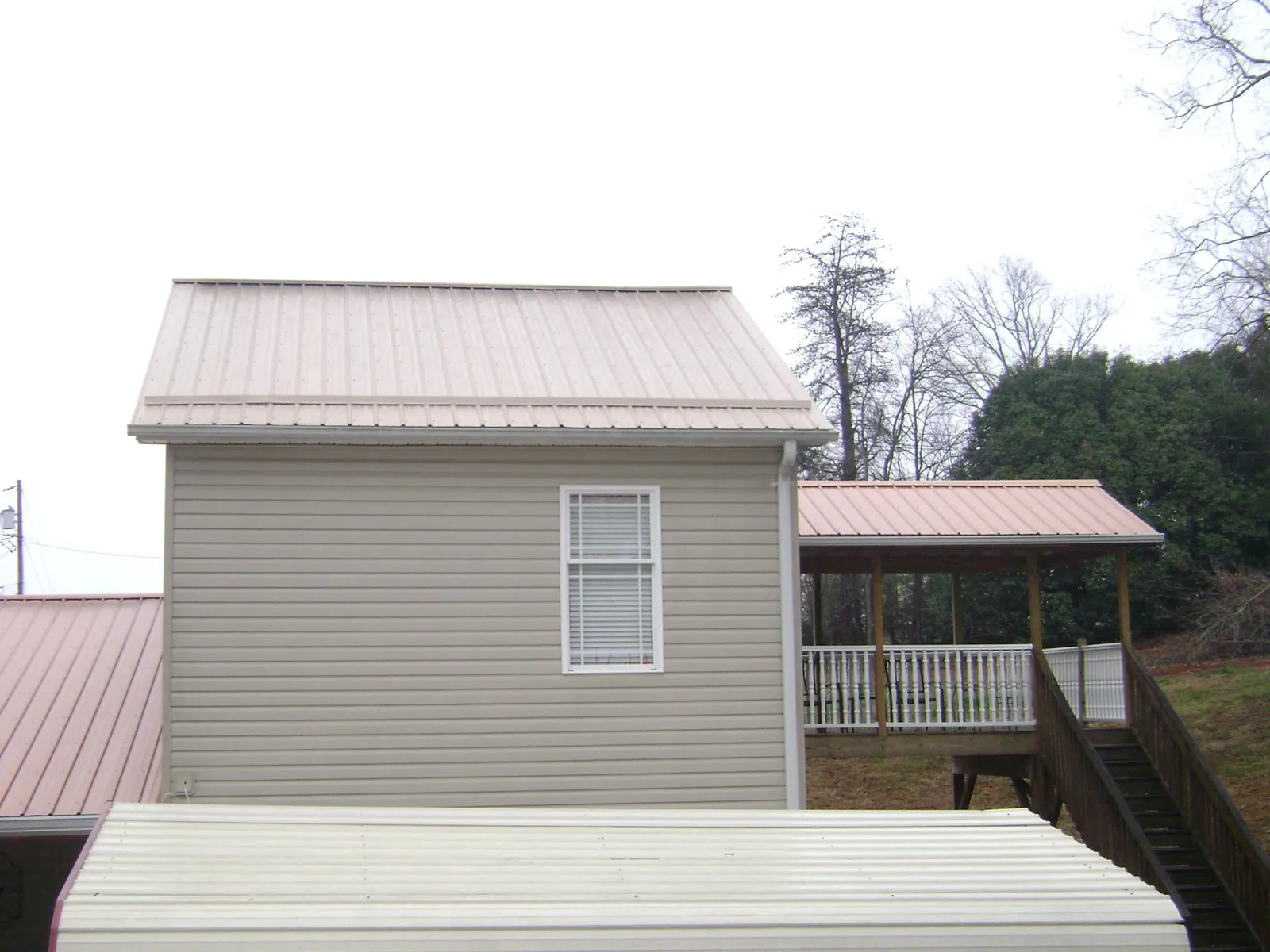 Tan metal roofs on a two story addition and attached porch, from a Roof Replacement job in Genoa